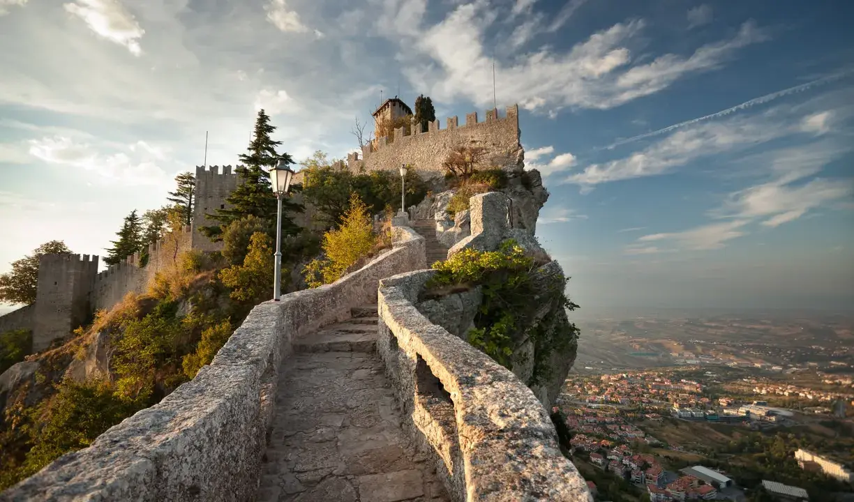 Sentiero in pietra che sale verso la Rocca della Guaita, simbolo di San Marino città, con vista panoramica sulla valle.