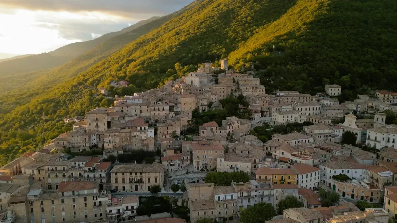 Borgo San Donato, un incantevole paese arroccato su un colle, immerso nel verde di una montagna illuminata dal sole al tramonto.
