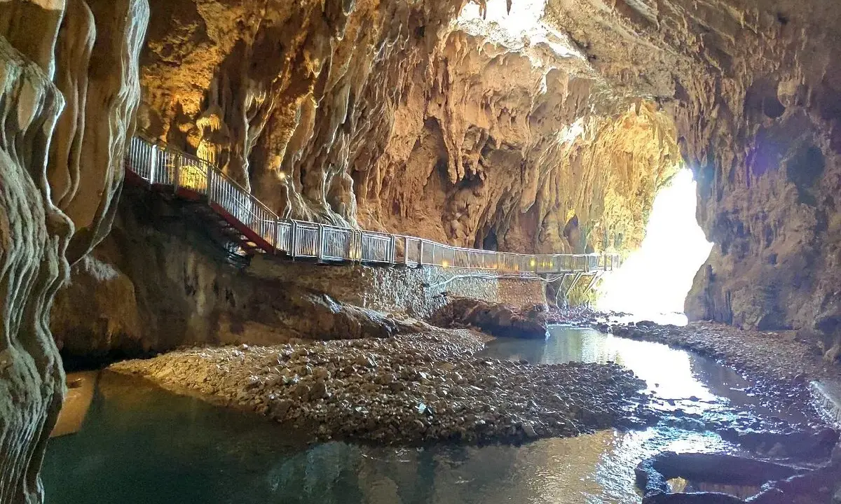 Sentiero illuminato lungo un ruscello nelle grotte di Pastena, tra stalattiti e stalagmiti dorate.
