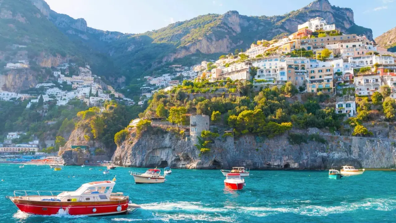 Barche a vela navigano nelle acque turchesi davanti alle case colorate aggrappate alle scogliere delle isole costiera amalfitana.