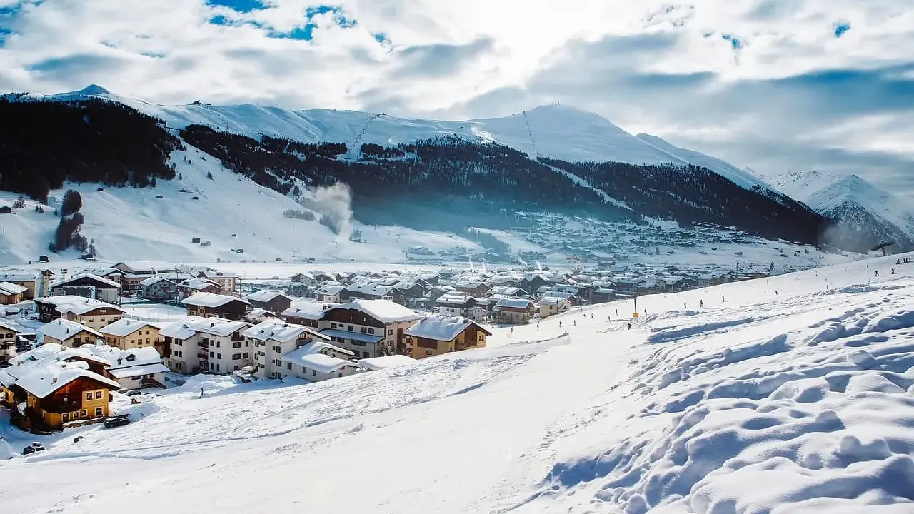 Paesaggio invernale con villaggio innevato e montagne sullo sfondo. Perfetto per sapere dove andare in montagna in Trentino per sciare.