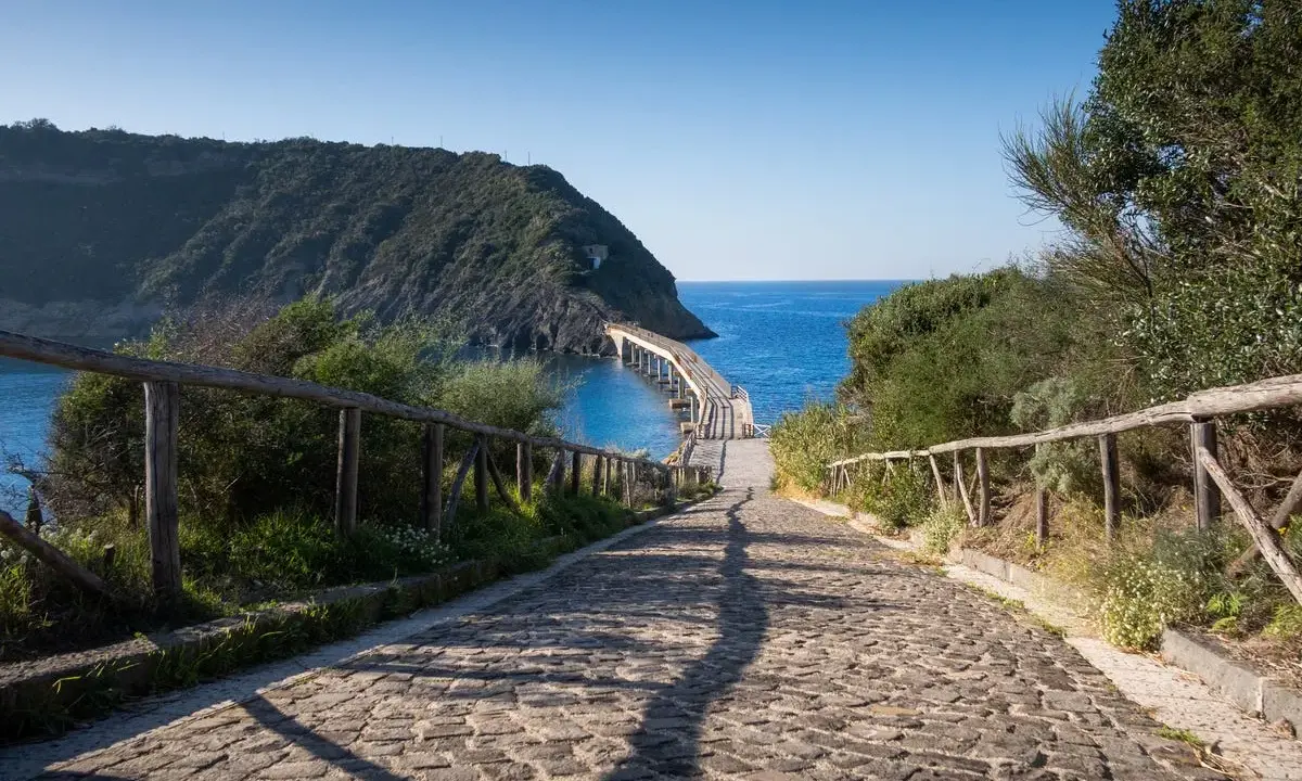 Sentiero acciottolato verso un ponte sul mare, ideale per cammini in Italia sul mare.