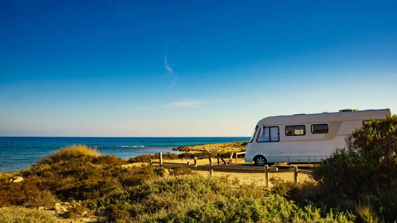 Un camper bianco sosta su un sentiero sabbioso con vista sul mare blu intenso. Un'avventura indimenticabile in camper all'Isola d'Elba.