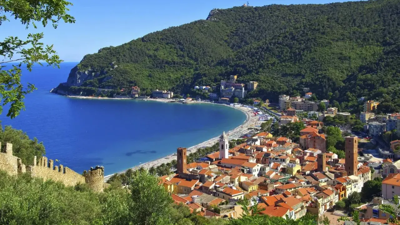 Vista panoramica di pittoreschi liguria paesi sul mare, con case dai tetti rossi che scendono verso una baia azzurra e una spiaggia affollata.