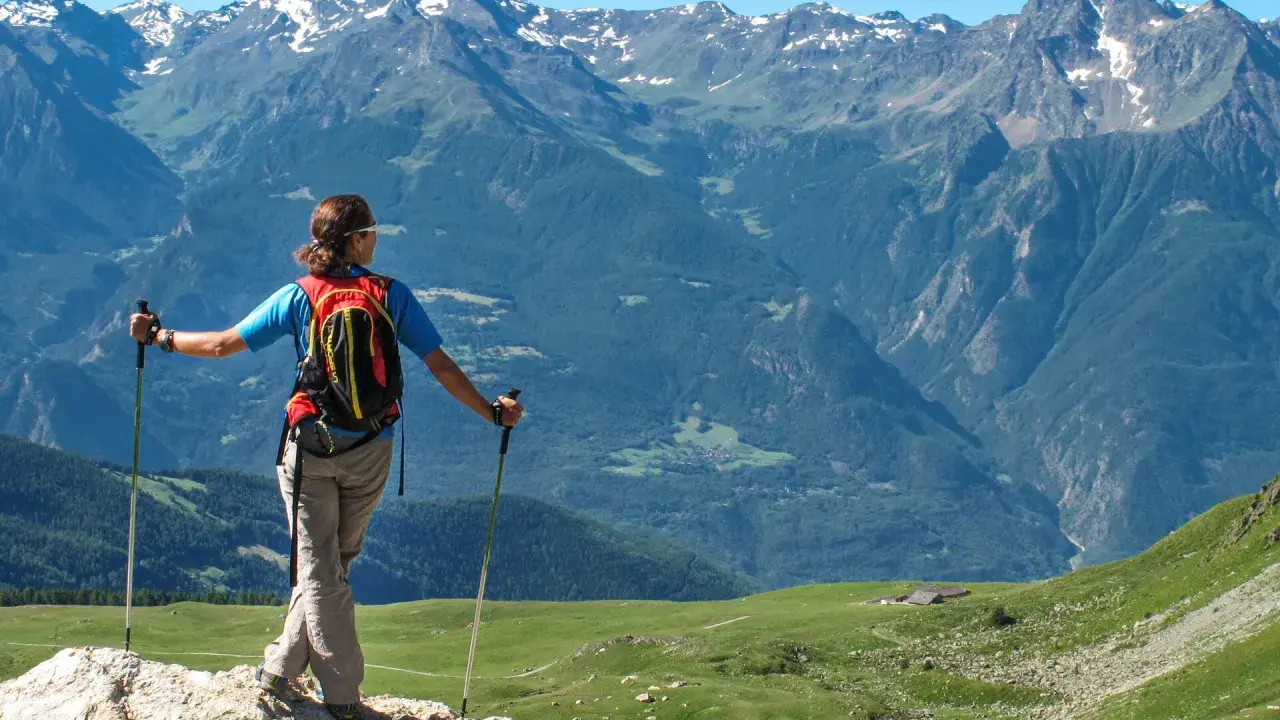 Escursionista con zaino e bastoncini ammira un panorama alpino mozzafiato, perfetto per scoprire gli itinerari della Valle d'Aosta.