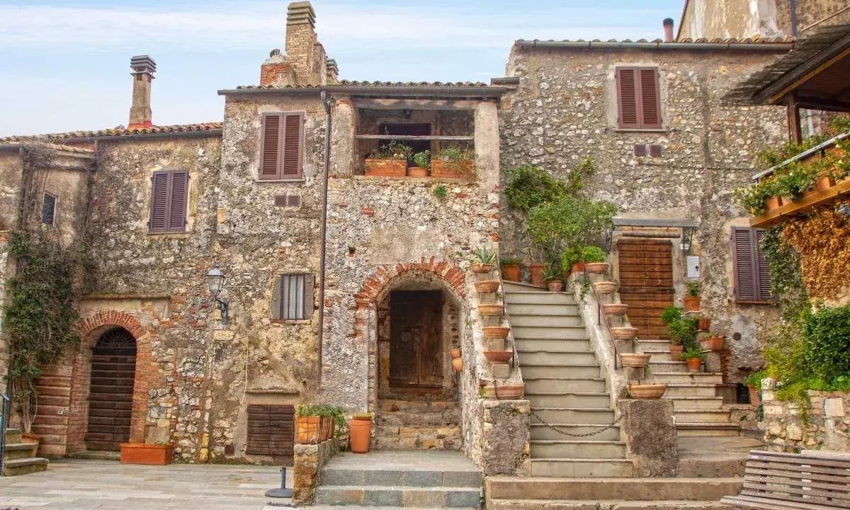 Antica piazza con case in pietra, scale in terracotta e piante rigogliose, un'atmosfera da **borghi medievali toscana**.