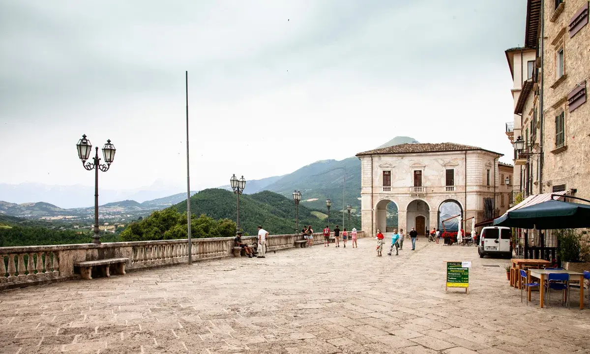 Piazza di Civitella del Tronto con edifici storici, gente che passeggia e vista panoramica sulle colline verdi.