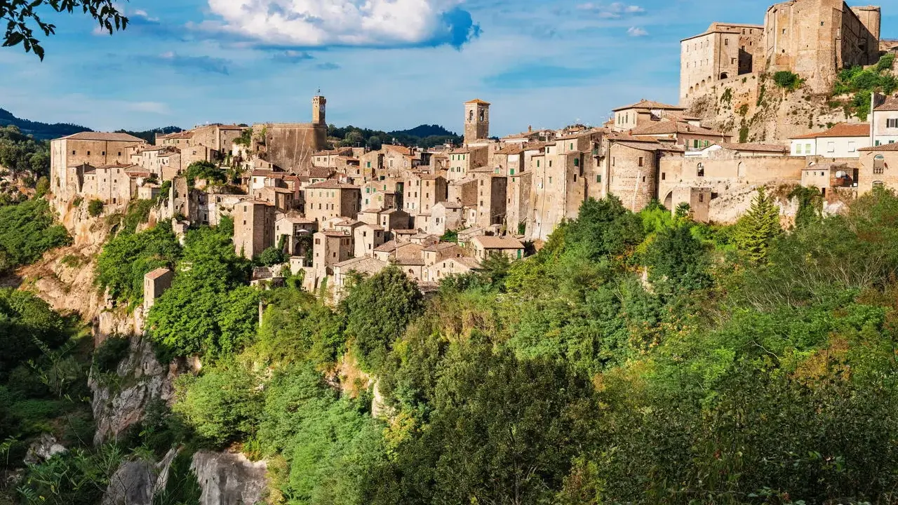 Un affascinante borgo toscano da visitare, arroccato su una rupe tufacea, con case in pietra e torri che si stagliano contro il cielo azzurro.