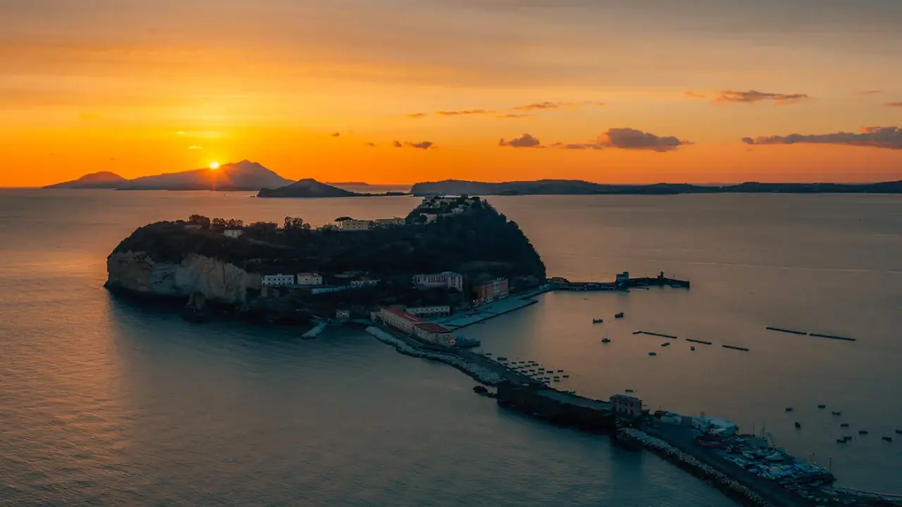 Tramonto infuocato sul golfo di Napoli, con una suggestiva isoletta che emerge dal mare calmo, illuminata dagli ultimi raggi dorati.