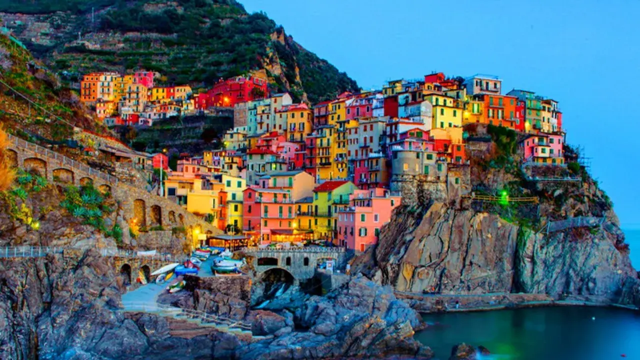 Case colorate aggrappate alla scogliera, un incantevole scorcio di quali sono le 5 Terre, con barche ormeggiate e il mare blu.