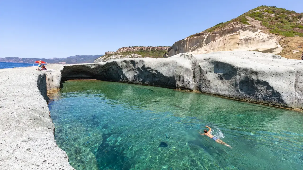 Un uomo nuota in acque cristalline tra scogliere bianche. Un luogo ideale per scoprire le spiagge di Bosa e cosa vedere.