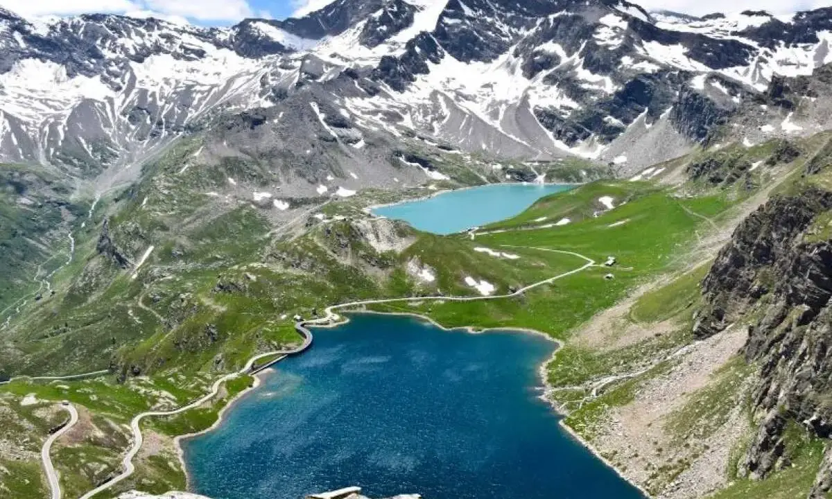 Laghi alpini blu e turchese ai piedi del Colle del Nivolet, con strade tortuose e montagne innevate sullo sfondo.