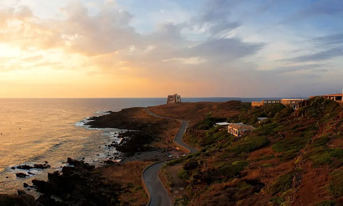 Torre di tramontana e case sparse su una collina, con mare e cielo al tramonto. Ecco cosa vedere a Ustica per un'esperienza indimenticabile.