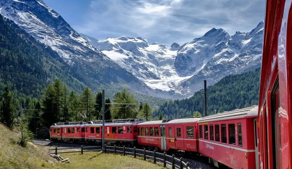 Treni panoramici rossi attraversano un paesaggio alpino mozzafiato con montagne innevate e foreste verdi.