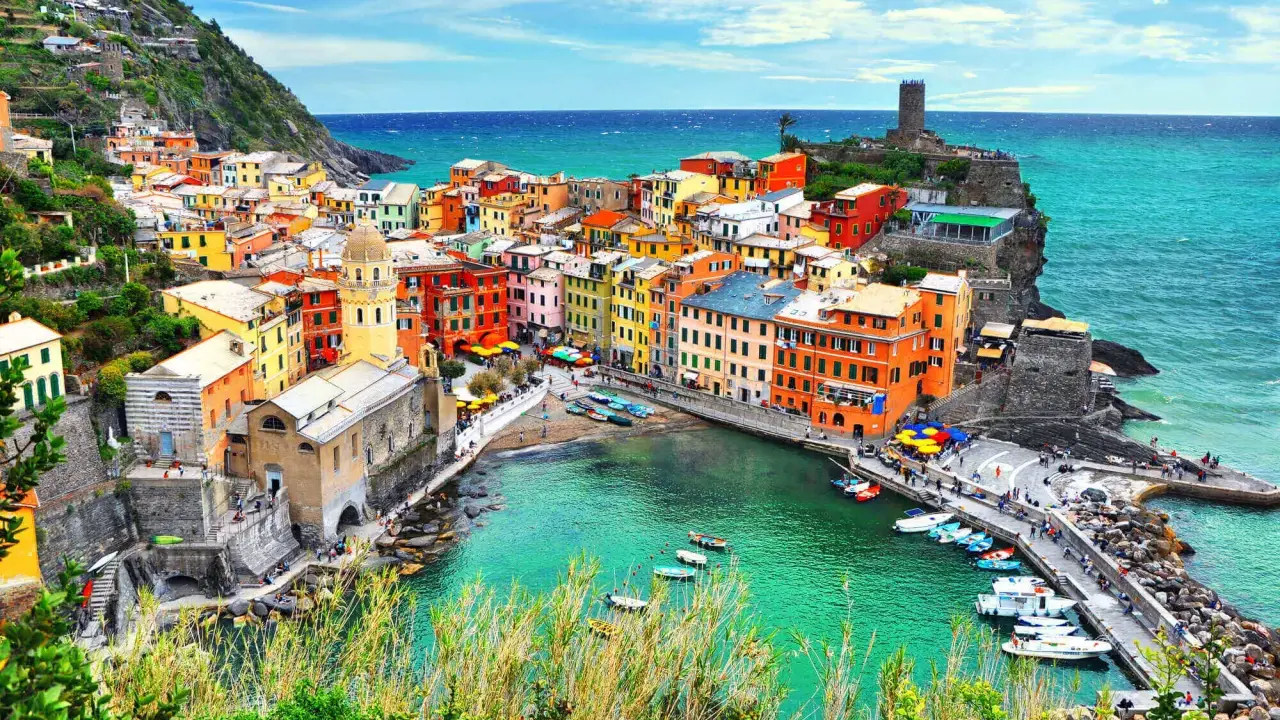 Le Cinque Terre, un gioiello colorato aggrappato alla costa, con case vivaci che si affacciano sul mare turchese e barche che ondeggiano nel porto.