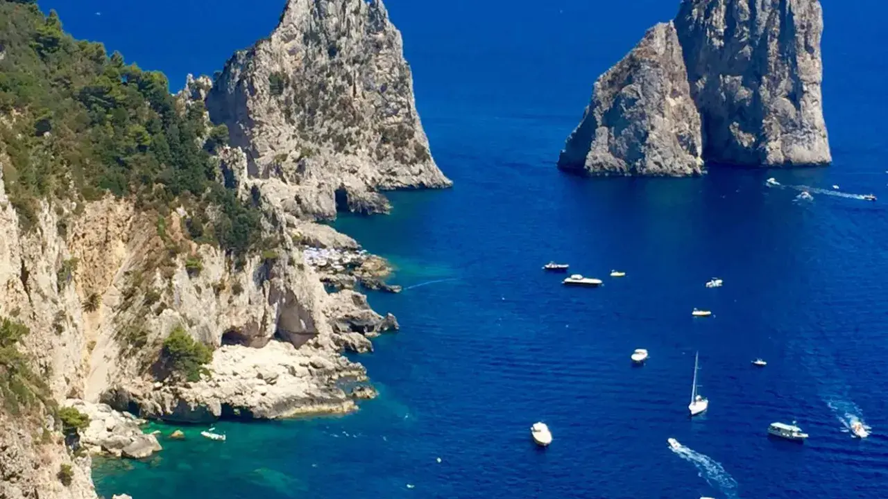 Faraglioni di Capri, tra le più belle isole di Napoli da visitare. Barche navigano nel mare blu intenso.