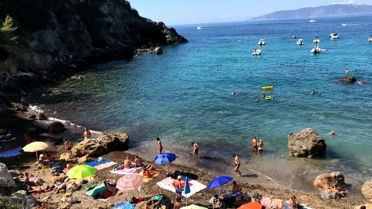 Spiaggia affollata con ombrelloni colorati e gente che nuota. Ecco come arrivare a Cala del Gesso per godersi questo mare cristallino.