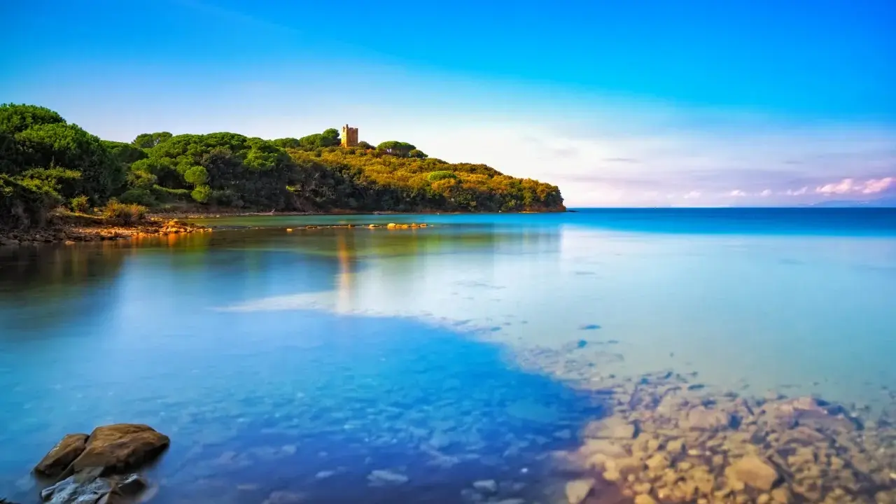 Torre medievale su una collina verdeggiante, con acque cristalline che lambiscono le **punta ala spiagge più belle**.