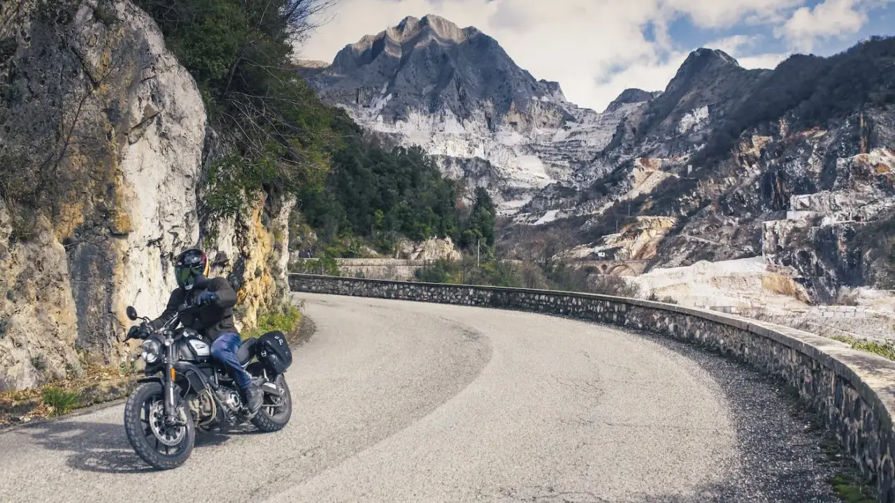 Motociclista su strada tortuosa con montagne di marmo sullo sfondo, un'autentica **Toscana da visitare**.