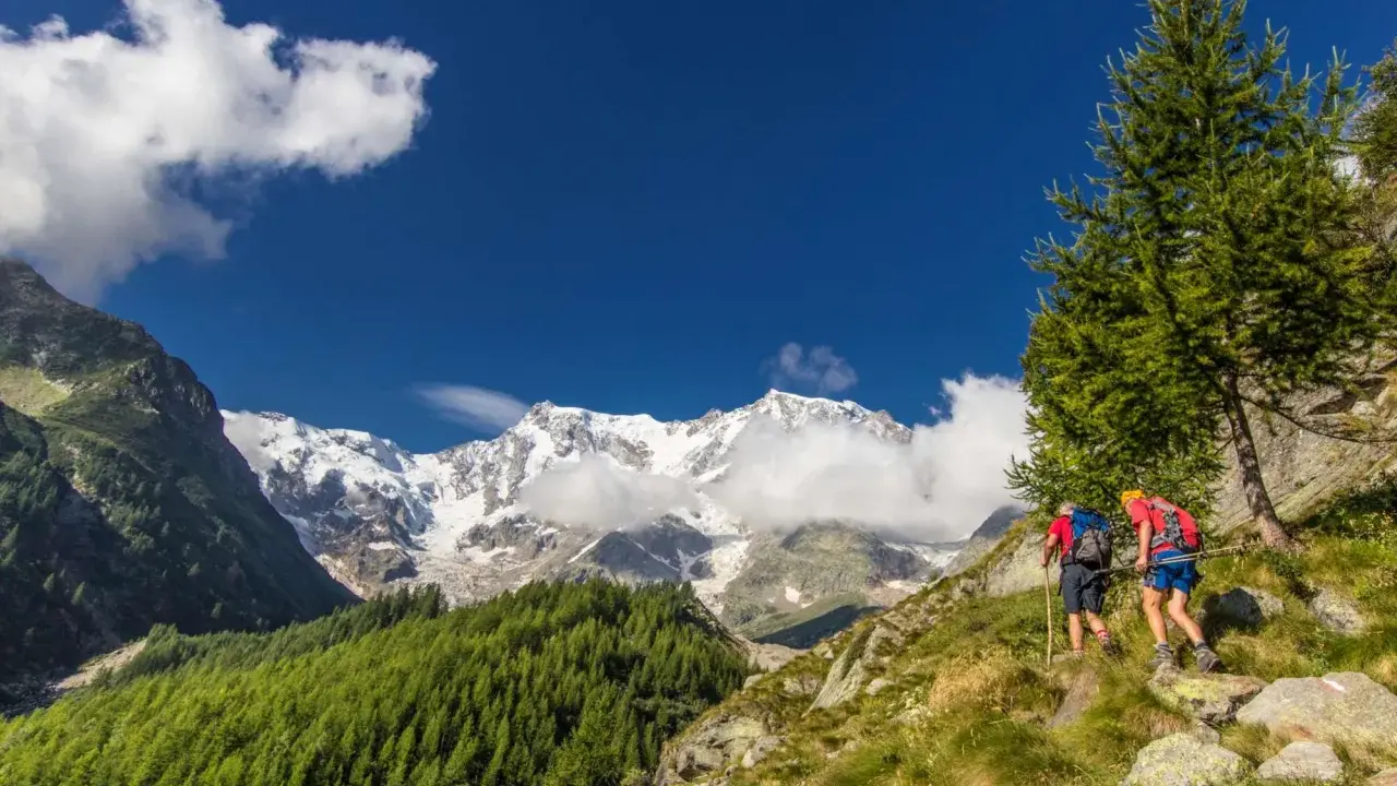 Due escursionisti affrontano un sentiero in Val d'Ossola, con maestose cime innevate sullo sfondo. Perfetto per escursioni facili.