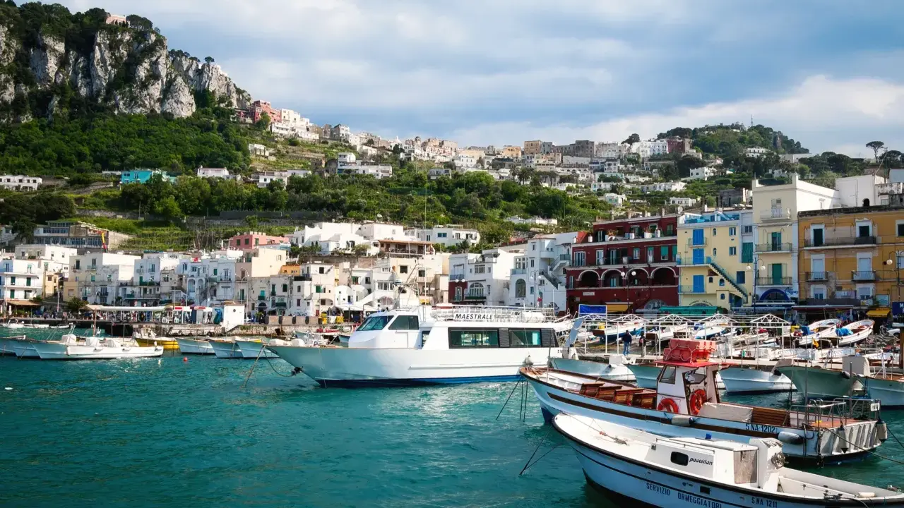 Barche nel porto di Capri, con la città arroccata sulla collina. Un ottimo punto di partenza per capire come raggiungere Capri da Napoli.