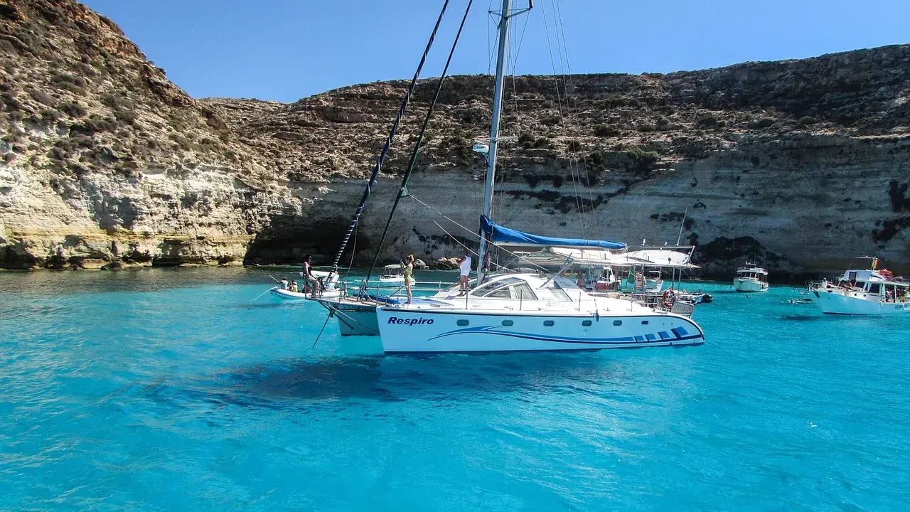 Catamarano "Respiro" in acque cristalline di un'isola sotto la Sicilia, con scogliere rocciose e altre barche.