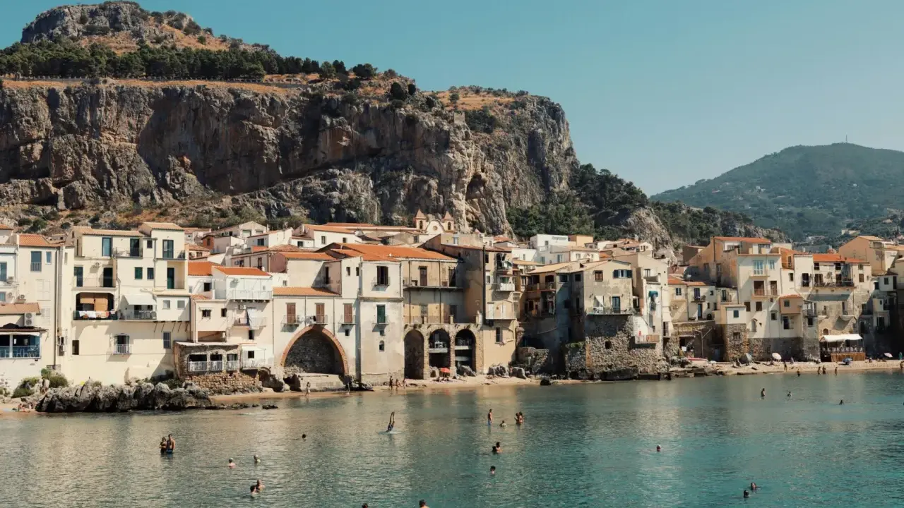 Un incantevole borgo da visitare in Sicilia, con case color pastello affacciate sul mare cristallino e una maestosa roccia a fare da sfondo.