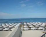 Spiaggia di **Marina di Follonica** con file ordinate di ombrelloni bianchi, mare azzurro e cielo sereno.