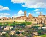 Panoramica di Volterra, dove si trova questo antico borgo toscano, con le sue torri e case arroccate sulla collina sotto un cielo azzurro con nuvole bianche.