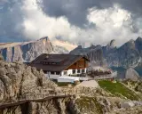 Rifugio alpino con terrazza panoramica, uno dei migliori rifugi dove dormire Dolomiti, incastonato tra imponenti vette rocciose e nuvole minacciose.