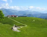 Un sentiero delle malghe serpeggia tra verdi colline, conduce a rustici edifici e si perde tra le montagne nebbiose.