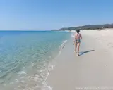 Un bambino cammina su una spiaggia di sabbia bianca, verso le spiagge più belle della Sardegna est. Acqua cristallina e cielo azzurro.