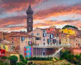 Un borgo italiano con case colorate e una torre campanaria, sotto un cielo infuocato. Potrebbe essere qual è il borgo più bello d'Italia.