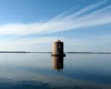Mulino solitario nella laguna di Orbetello, con cielo azzurro e nuvole sottili.