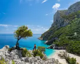 Escursionista ammira una baia cristallina con una spiaggia bianca, incastonata tra imponenti scogliere verdi. Un paesaggio mozzafiato che ricorda la bellezza della montagna centro Italia.