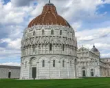 Il Battistero, il Duomo e la Torre Pendente: ecco cosa vedere a Pisa in un giorno, un'iconica piazza con un prato verde e cielo nuvoloso.
