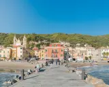 Laigueglia centro storico: case colorate affacciate sulla spiaggia, con una chiesa a due campanili e il mare azzurro.