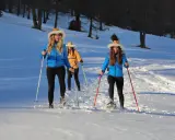 Tre amiche si godono escursioni invernali nelle Dolomiti Bellunesi, camminando sulla neve con le ciaspole e bastoncini.