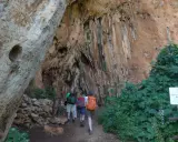Escursionisti esplorano un sentiero nella Riserva dello Zingaro, avvicinandosi a un'imponente parete rocciosa con vegetazione rigogliosa.