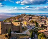 Un borgo medievale arroccato su una collina, tra i più belli d'Italia, con un castello imponente e case in pietra sotto un cielo azzurro.