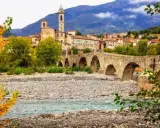 Ponte Gobbo a Bobbio, borgo dei borghi, con il fiume e le montagne sullo sfondo.