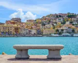 Panoramica di Porto Santo Stefano con case colorate a picco sul mare turchese. Un invito a scoprire cosa vedere a Porto Santo Stefano.