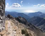 Sentiero roccioso su un crinale montuoso, con vista sul mare e sulle colline. Un percorso che ricorda la via Vandelli, un'antica strada panoramica.