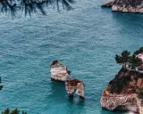 Scogliere mozzafiato e spiagge deserte Italia, con faraglioni che emergono dal mare turchese e una villa panoramica.
