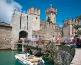 Castello Scaligero di Sirmione, un'ottima idea per cosa vedere a Sirmione in un giorno. Un ponte pedonale affollato porta all'ingresso del castello, con un motoscafo ormeggiato nell'acqua turchese.