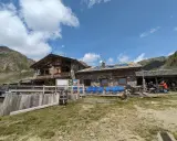Rifugio Mont Fallère, uno dei rifugi Valle d'Aosta facili, accoglie escursionisti con le sue strutture in pietra e legno, circondato da verdi pendii e montagne.