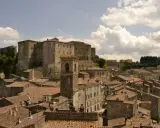 Panoramica di antichi borghi vicino Follonica, con un imponente castello in cima alla collina e un campanile che svetta tra i tetti rossi.
