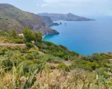 Panoramica mozzafiato per capire come visitare le Isole Eolie: costa verdeggiante, mare blu intenso e isole vulcaniche all'orizzonte.