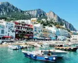Colorate case affacciate sul mare turchese, con barche ormeggiate e montagne sullo sfondo. Un incantevole scorcio delle isole vicino Napoli.