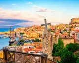 Una statua con una croce domina la vista di una città costiera colorata, perfetta per una gita fuori porta da Roma.